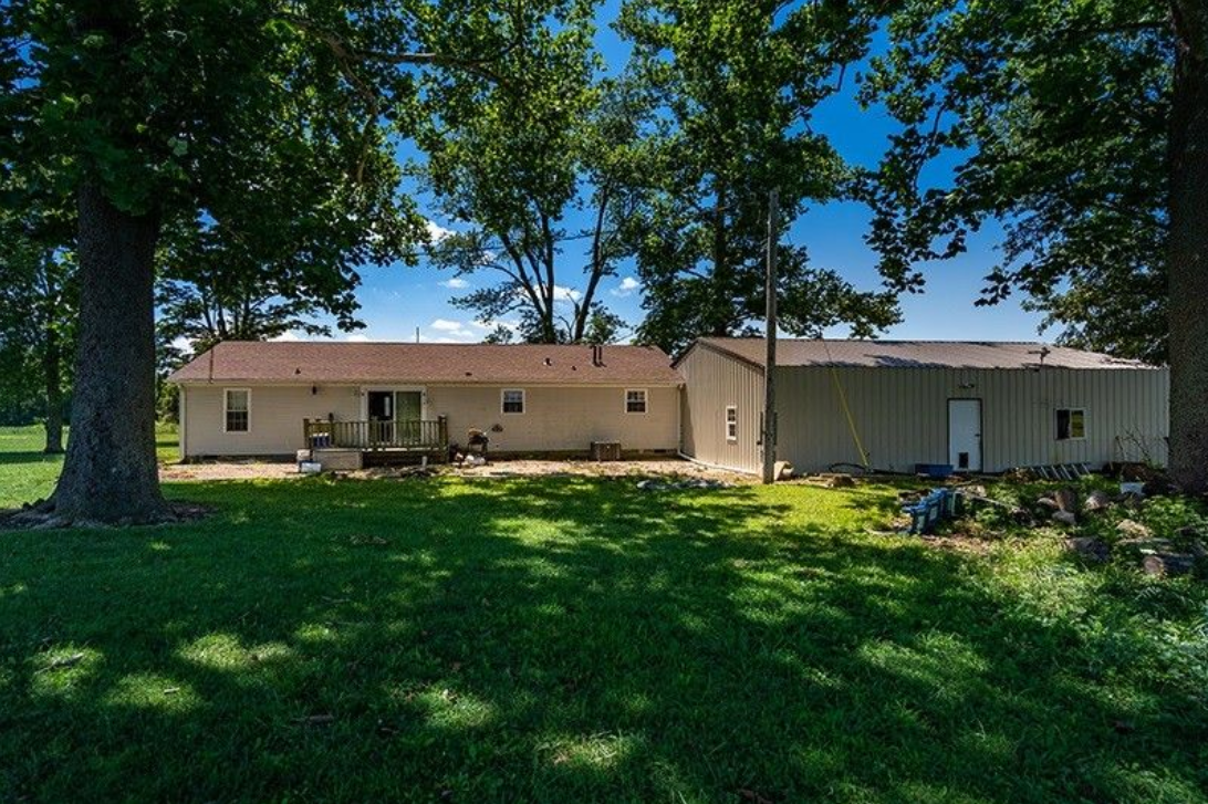 A large white house is sitting on top of a lush green field surrounded by trees.