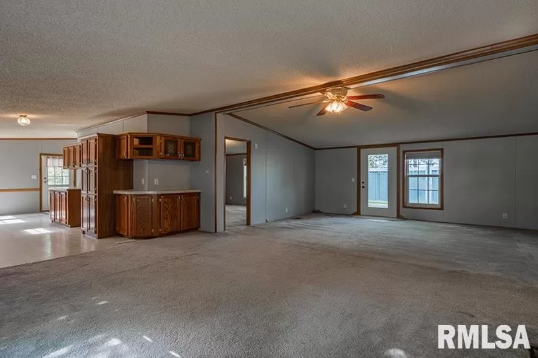 A large empty room with a ceiling fan in a mobile home.