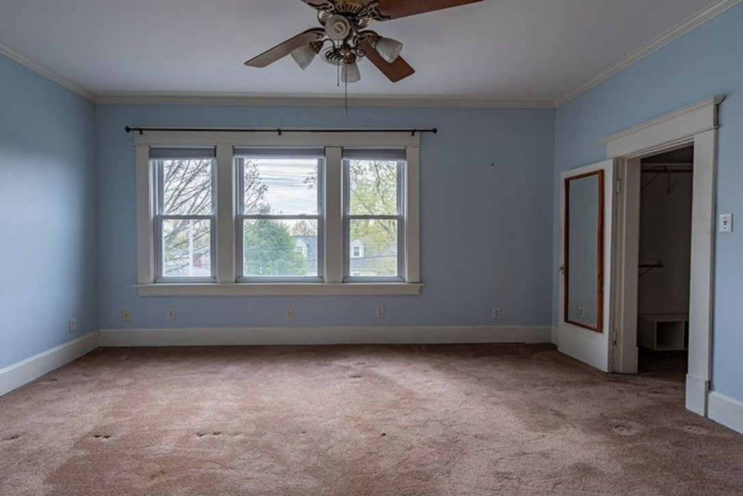 An empty room with blue walls and a ceiling fan.