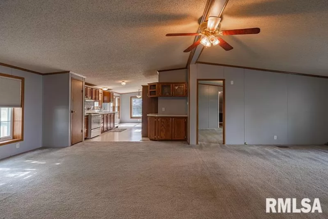 A large empty room with a ceiling fan in a mobile home.
