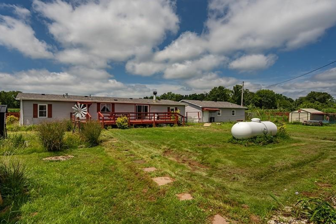 There is a propane tank in the grass in front of a house.