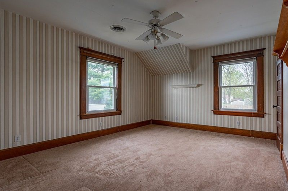 An empty room with a ceiling fan and two windows.