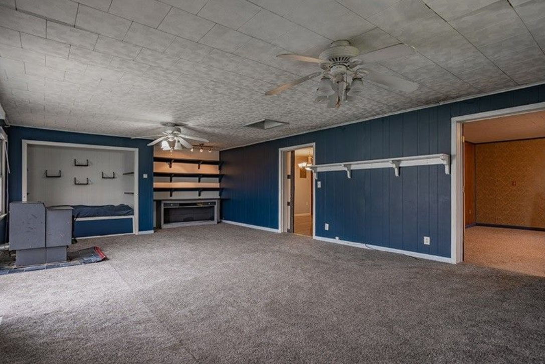 An empty living room with blue walls and a ceiling fan.