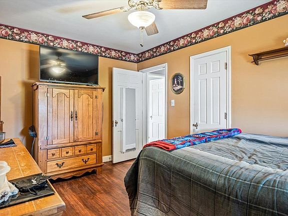 A bedroom with a bed , dresser , television and ceiling fan.