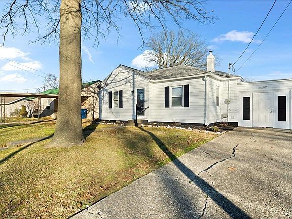 A white house with a tree in front of it and a driveway.