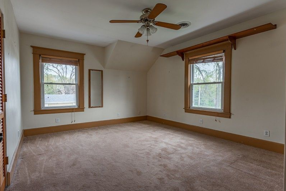 An empty bedroom with a ceiling fan and two windows.
