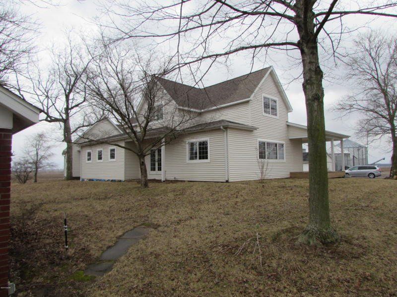 A white house with a brown roof sits in the middle of a grassy field