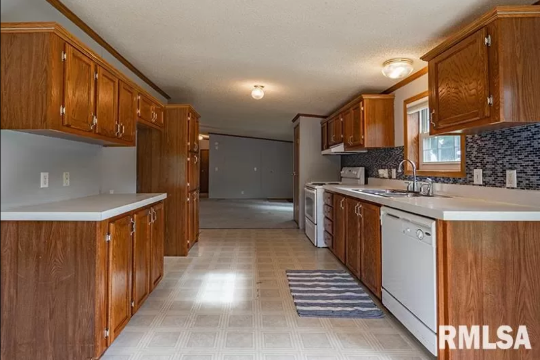 An empty kitchen with wooden cabinets and white appliances