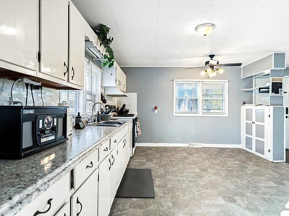 A kitchen with white cabinets , granite counter tops , a microwave and a window.