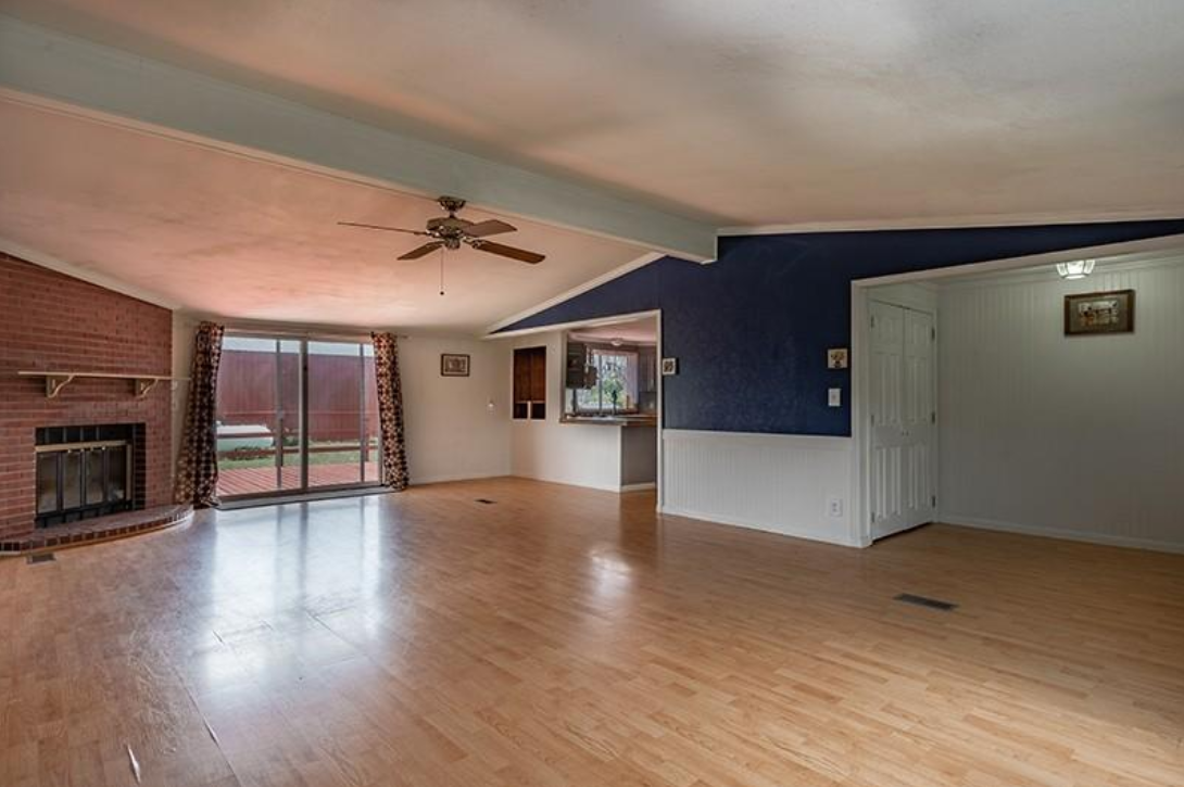 An empty living room with hardwood floors , a fireplace and a ceiling fan.