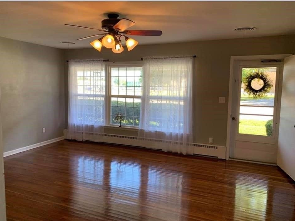 An empty living room with hardwood floors and a ceiling fan.