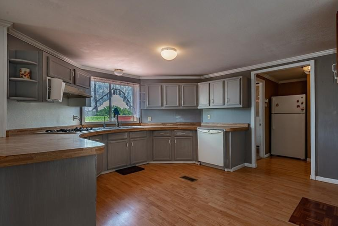 An empty kitchen with wooden floors and gray cabinets.