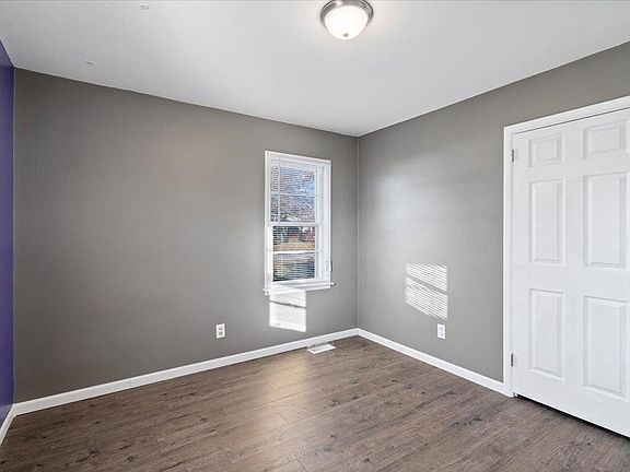 An empty room with gray walls and hardwood floors and a window.