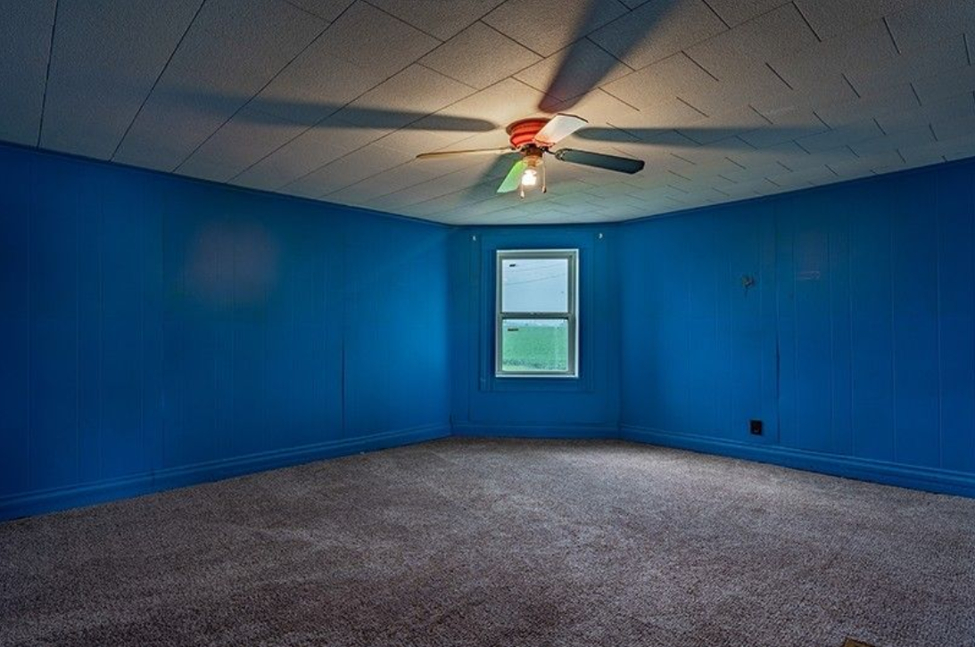 An empty room with blue walls and a ceiling fan.