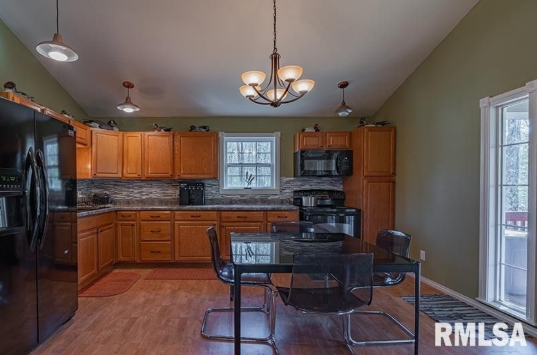 A kitchen with wooden cabinets , a black refrigerator , a table and chairs.