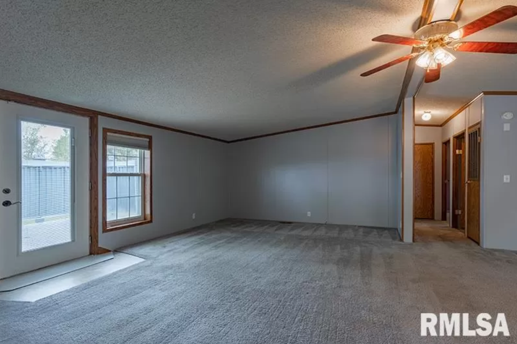An empty living room with a ceiling fan and a sliding glass door.