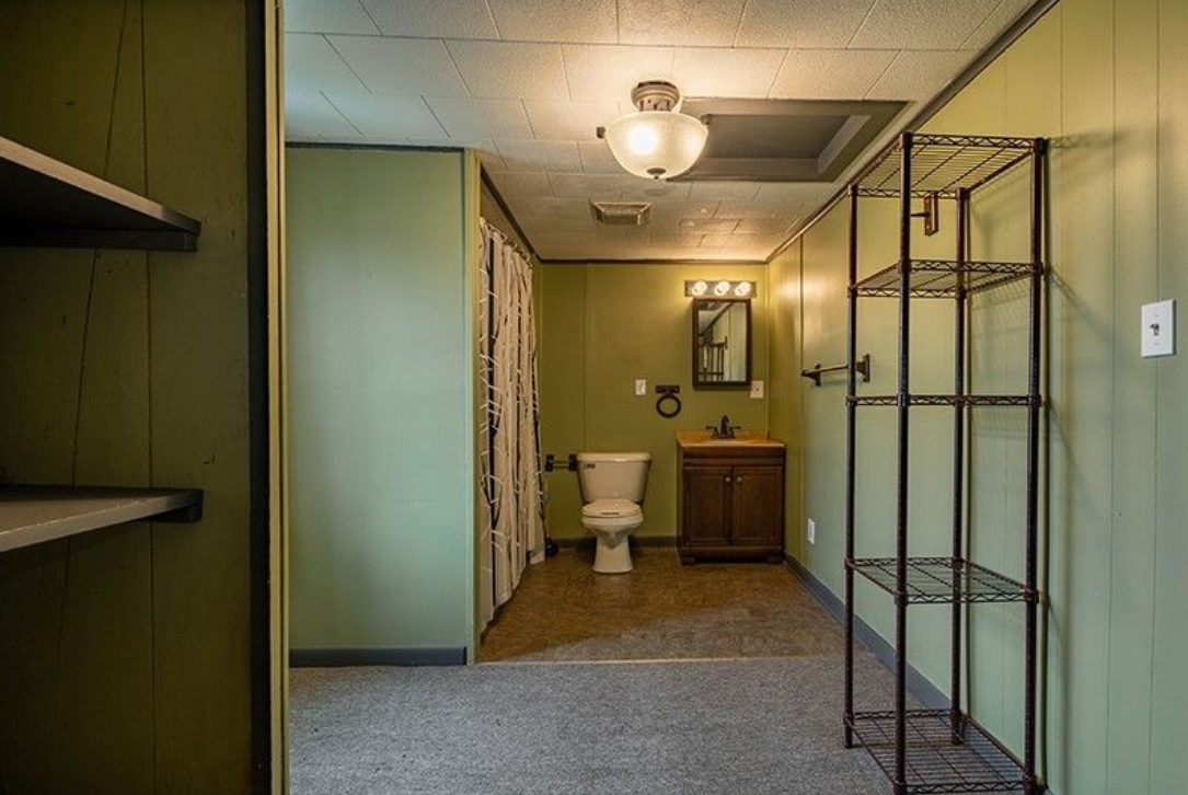A bathroom with a toilet , sink , mirror and shelves.