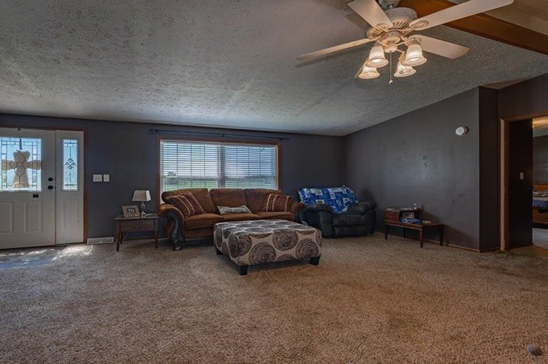 A living room with a couch , chairs , ottoman and ceiling fan.