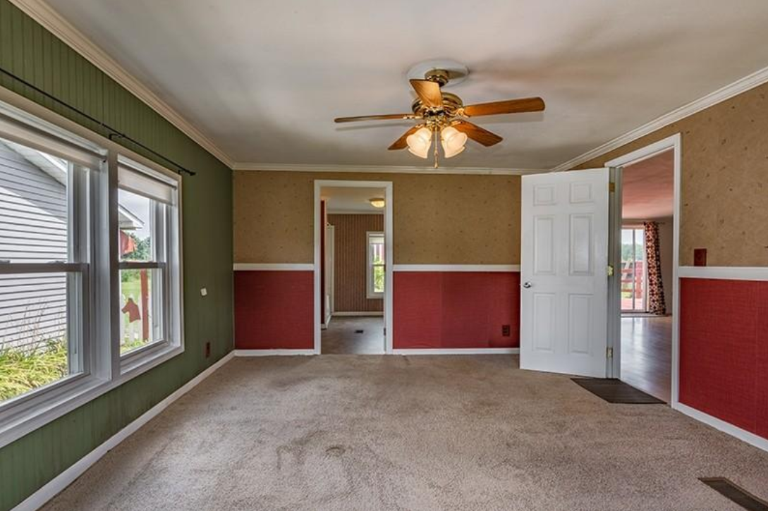 An empty living room with red and green walls and a ceiling fan.