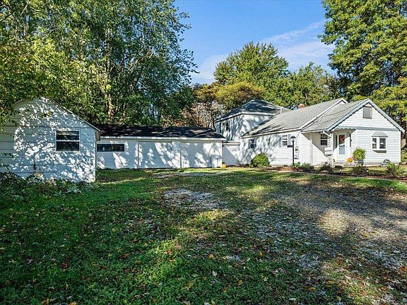 A white house is sitting on top of a lush green field surrounded by trees.