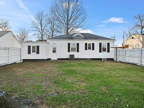 The backyard of a white house with a white fence and grass.