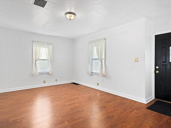 An empty living room with hardwood floors and white walls.