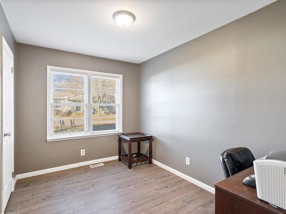 A room with a desk , chair , and two windows.