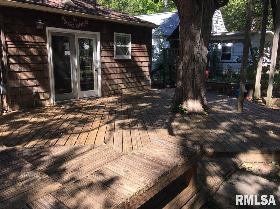 A wooden deck in front of a house with a tree in the background.