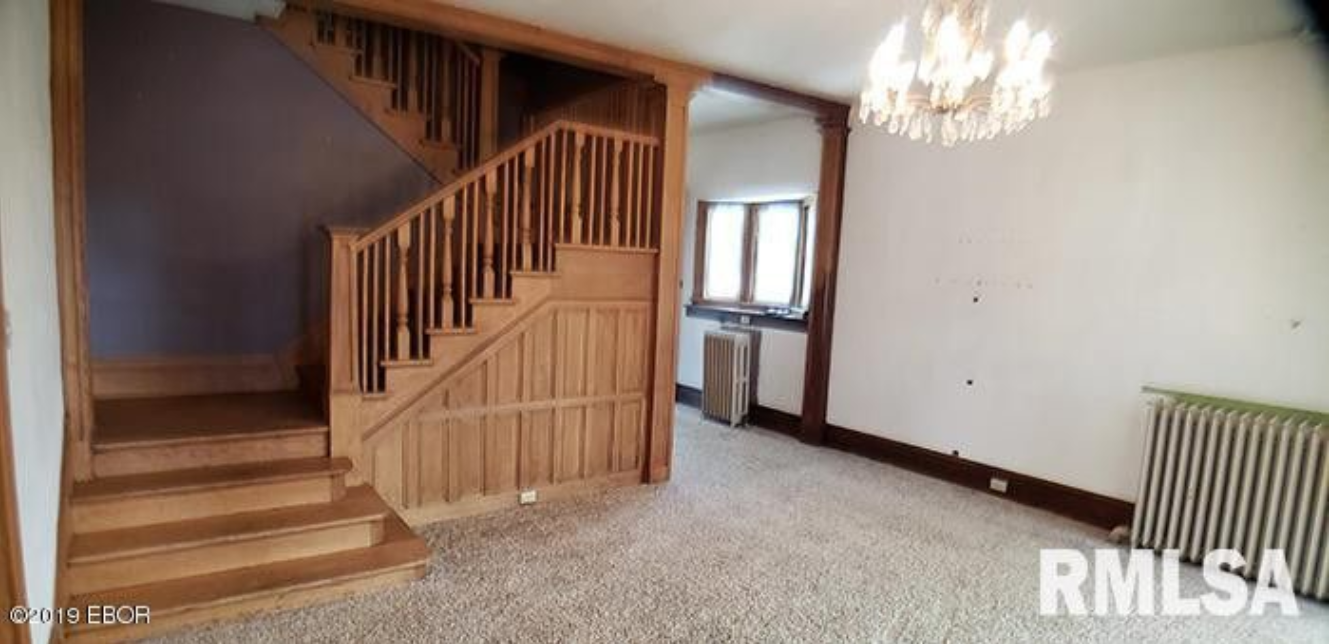 An empty living room with a wooden staircase and a chandelier.