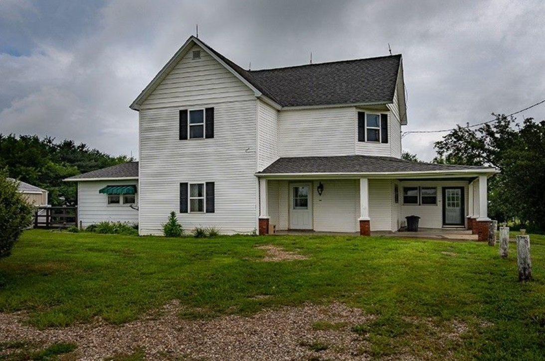 A white house with a gray roof is sitting on top of a lush green field.
