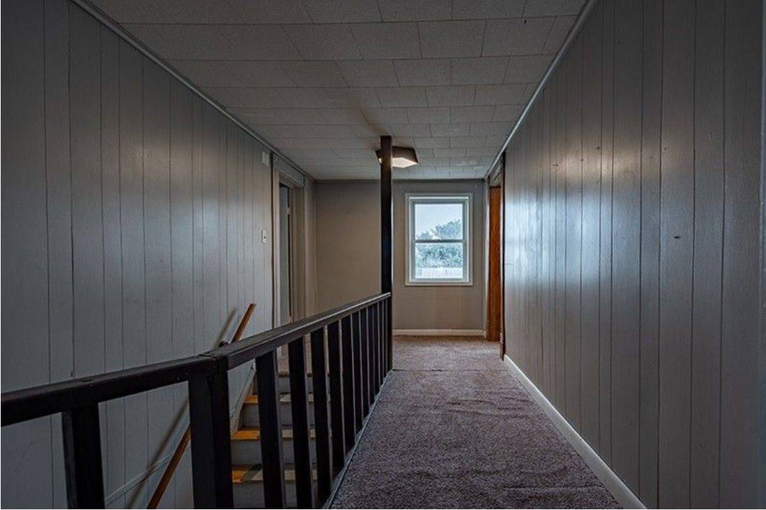 A long hallway with stairs and a window in a house.
