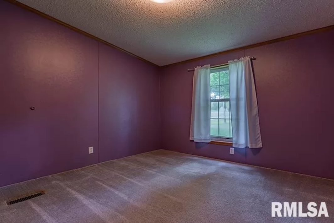 An empty bedroom with purple walls and a window.