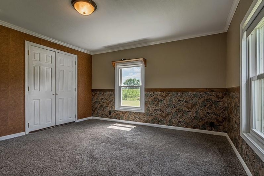 An empty room with a carpeted floor and two windows.
