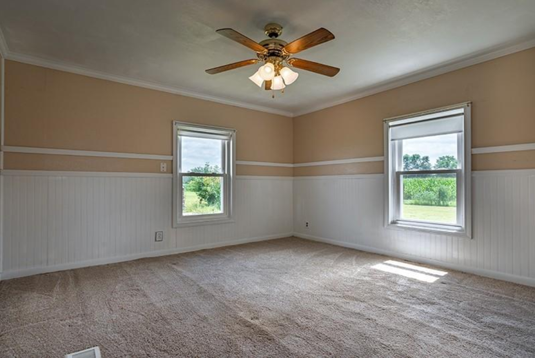 An empty bedroom with a ceiling fan and two windows.