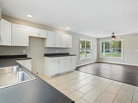 A kitchen with white cabinets , a sink , and a ceiling fan.