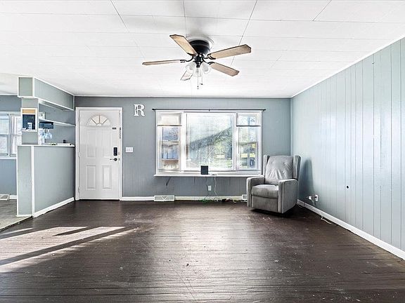 An empty living room with a ceiling fan and a chair.