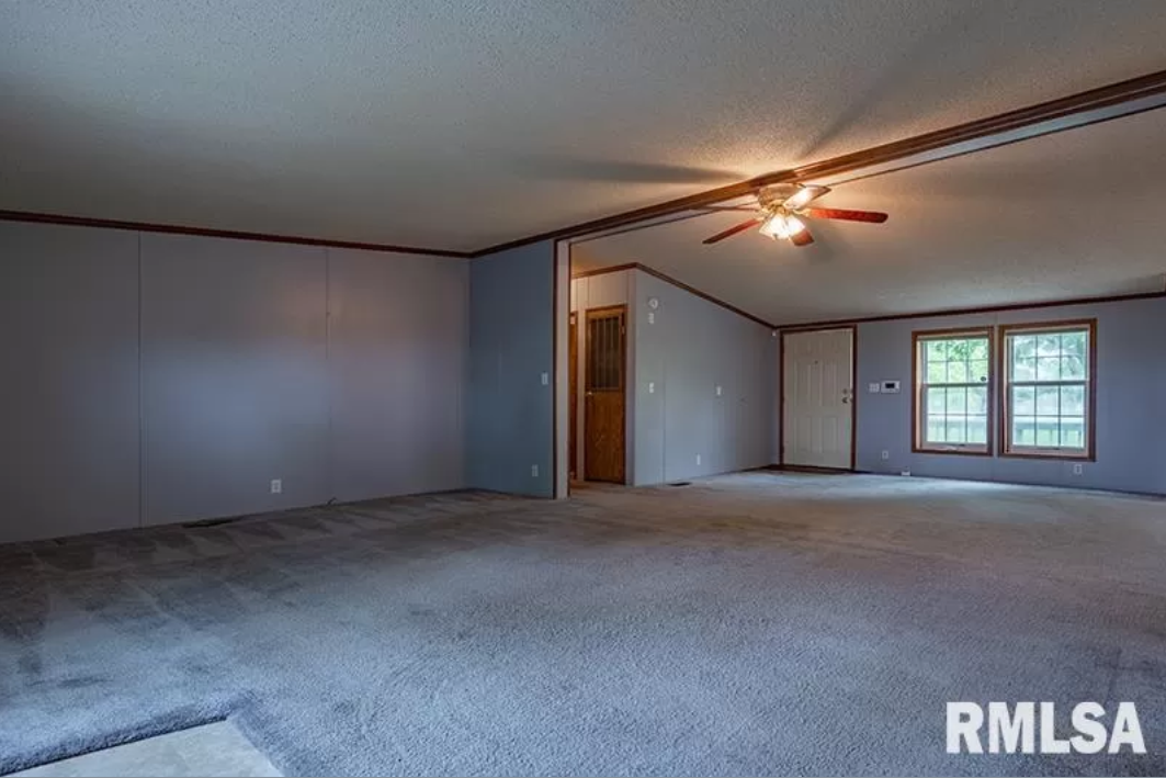 An empty living room with a ceiling fan and a large carpet.