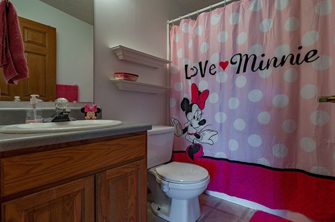 A bathroom with a toilet , sink , and shower curtain with minnie mouse on it.