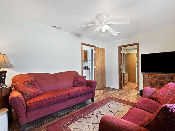 A living room with a red couch , two chairs , a television and a ceiling fan.