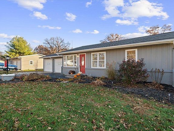 A gray house with a red door and a blue truck parked in front of it.