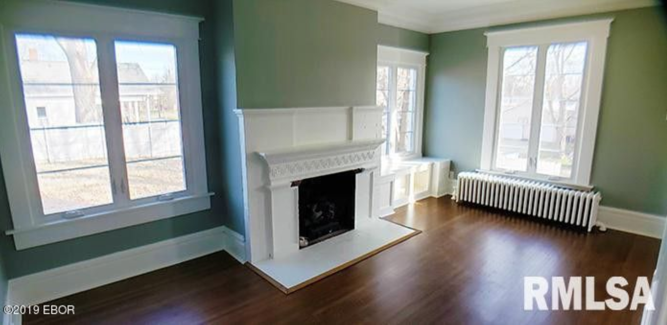 An empty living room with a fireplace and windows.