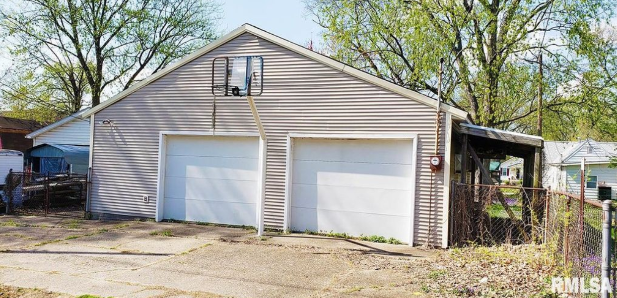 A garage with two white garage doors is sitting next to a house.