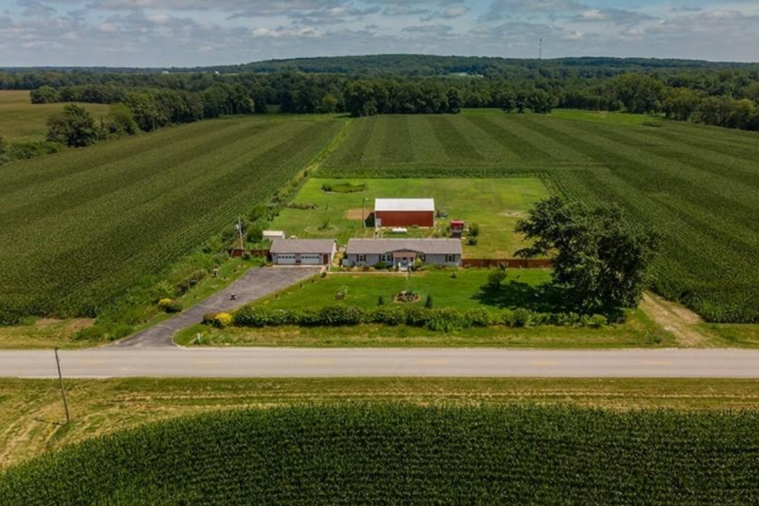 An aerial view of a farm with a red barn and a house in the middle of a field.