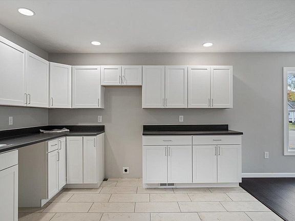An empty kitchen with white cabinets and black counter tops.