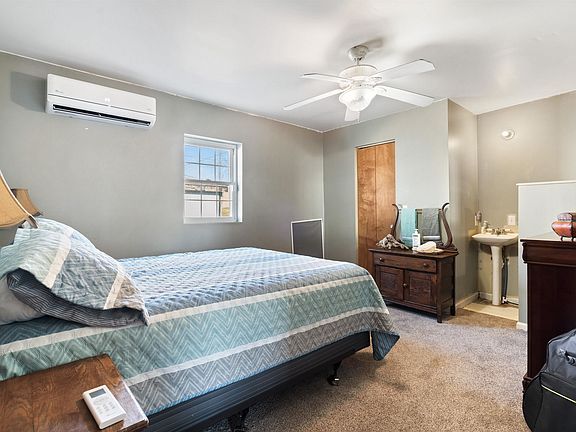 A bedroom with a bed , dresser , sink and ceiling fan.