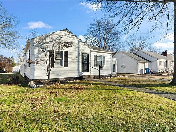 A small white house is sitting on top of a lush green hill.