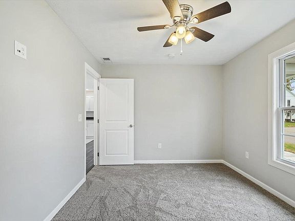 An empty bedroom with a ceiling fan and a window.