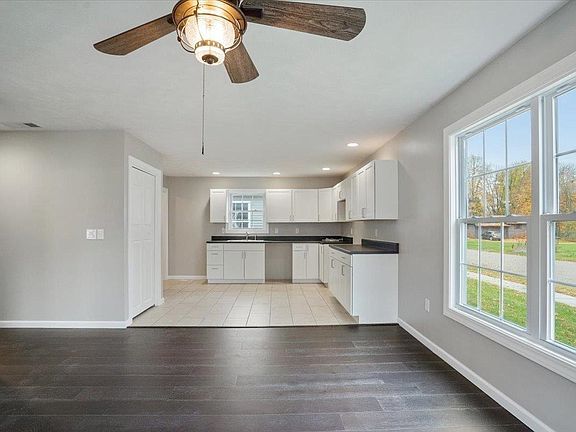 An empty room with a ceiling fan and a kitchen in the background.