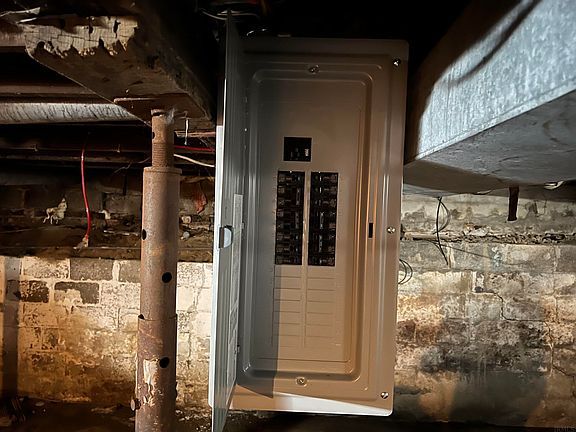A electrical box is sitting under a brick wall in a basement.