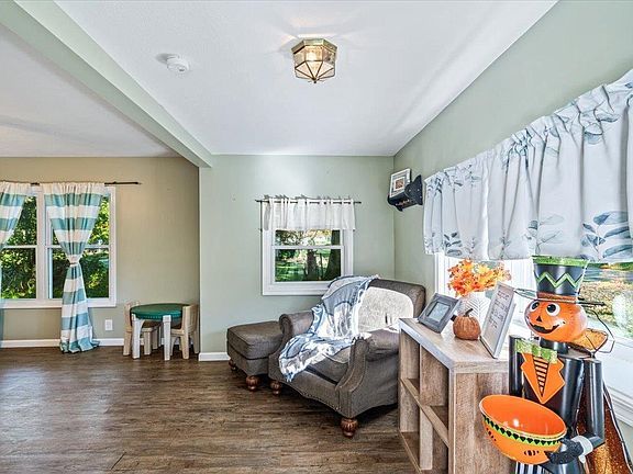 A living room with a chair , ottoman , table and windows.